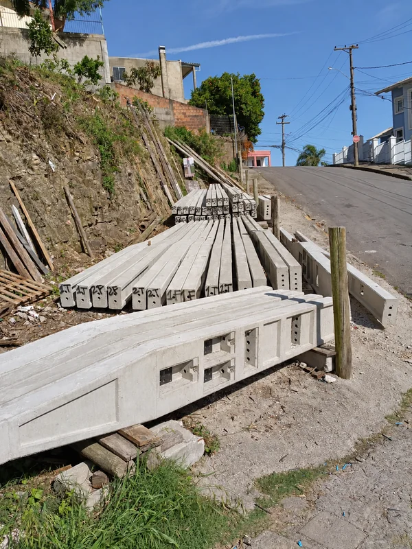 Postes de concreto armazenados em área externa.
